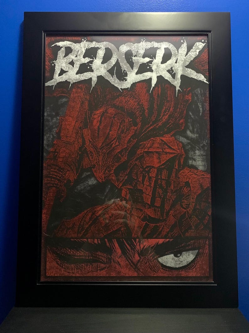 May include: A framed print of a black and white illustration of a character from the manga series Berserk. The character is wearing a helmet and armor. The title "Berserk" is written in silver lettering at the top of the print.