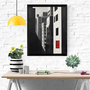 Puede incluir: Lámina de arte de paisaje urbano en blanco y negro en un marco negro. La obra de arte representa edificios altos con una sola ventana roja. La impresión se exhibe sobre una mesa de madera con un fondo de pared de ladrillo blanco.