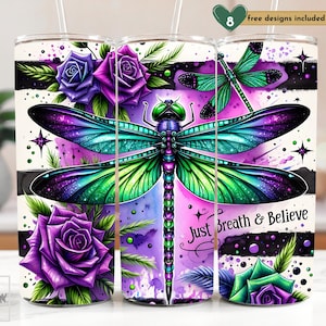 May include: A white tumbler with a purple, green, and black dragonfly design. The tumbler has the text "Just Breath & Believe" on it. The design also includes purple roses and a watercolor background.