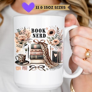 May include: White ceramic mug with a "BOOK NERD" design featuring books, coffee, and floral elements. The mug has a handle and is decorated with a stack of books, a coffee cup, and a scarf. The mug is available in 11 and 15oz sizes.