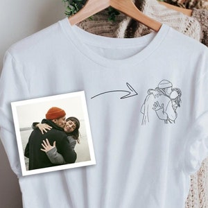 Könnte beinhalten: Weißes T-Shirt mit einer Strichzeichnung eines sich umarmenden Paares auf der Vorderseite. Links auf dem Shirt ist ein Foto eines sich umarmenden Paares mit einem Pfeil, der auf die Zeichnung zeigt.