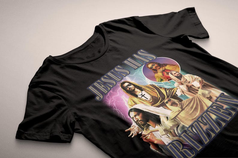 May include: Black t-shirt featuring a graphic design with the text "JESUS HAS RIZZEN" and images of Jesus. The design includes a cross, lightning bolts, and a circular image.