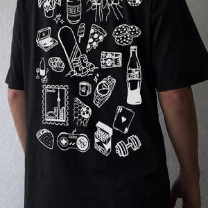 May include: Black t-shirt with a white graphic design featuring various icons such as a beer can, pizza slice, watch, and a video game controller. The shirt has a crew neck and short sleeves.