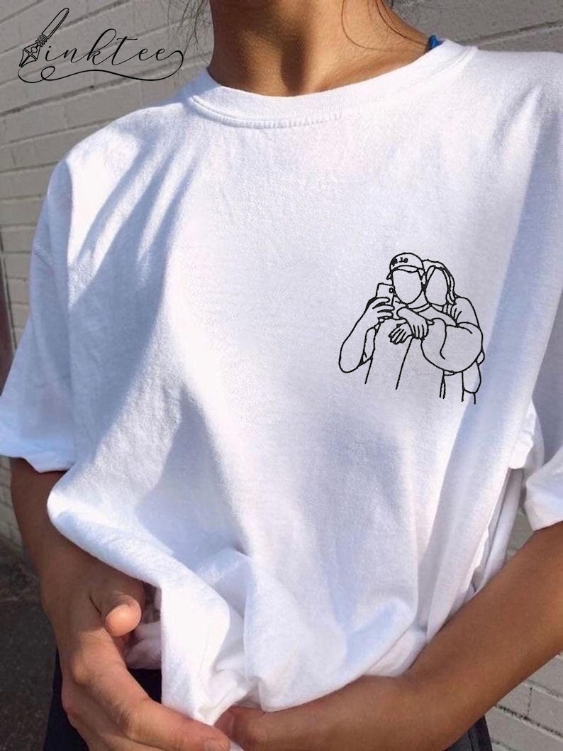 May include: White t-shirt with a small black line drawing of two people taking a selfie. The shirt has a crew neck and short sleeves. The brand name "inktee" is written in cursive in the upper left corner.