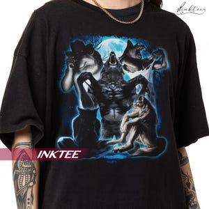 May include: Black t-shirt with a detailed graphic of wolves and a werewolf under a full moon. The design includes the text "INKTEE". The artwork uses shades of grey, blue, and white, creating a dramatic and detailed scene.