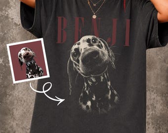 May include: A charcoal gray short-sleeve t-shirt featuring a large, detailed black and white graphic of a Dalmatian dog's face. Above the dog, the name BENJI is printed in bold, dark red capital letters. A small square inset shows the same dog.