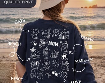 May include: A navy blue sweatshirt featuring a white graphic print on the back. The design includes the word MOM surrounded by various icons such as a cat, pizza slice, palm tree, suitcase, books, makeup brushes, and clothing items. The text #HIGH QUALITY PRINT is visible.