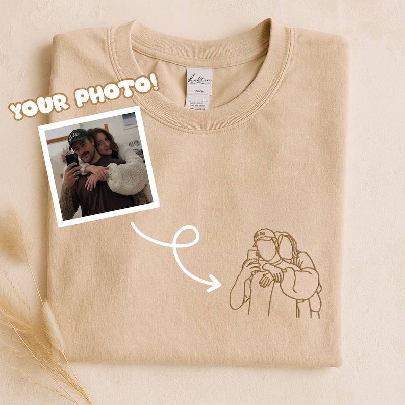 May include: A beige sweatshirt with a photo and line drawing of a couple. The photo is in a white frame and the line drawing is in brown. The text "YOUR PHOTO!" is in a brown, cartoon-style font.