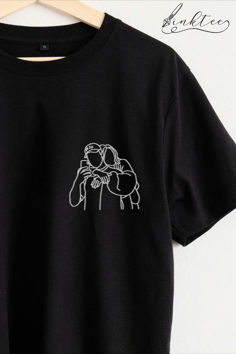 May include: Black t-shirt featuring a white line drawing of a couple taking a selfie. The design is on the left chest area. The shirt has short sleeves and a crew neck. The brand name "inktee" is written in cursive on the top right.