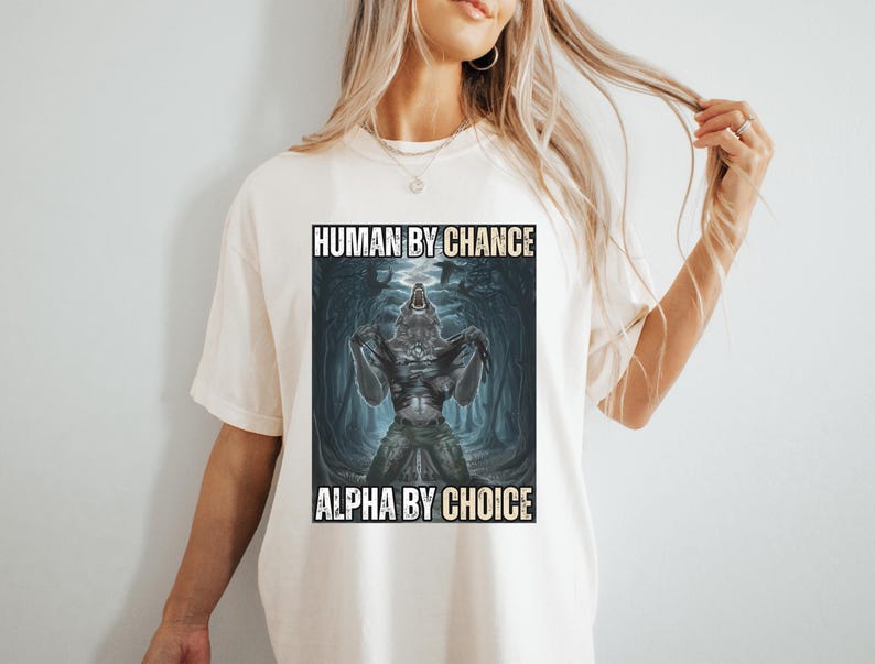 Puede incluir: Camiseta color crema con un gr&aacute;fico de un hombre lobo transform&aacute;ndose. La imagen est&aacute; ambientada sobre un fondo oscuro y cavernoso. El texto de la camiseta dice "HUMAN BY CHANCE" encima de la imagen y "ALPHA BY CHOICE" debajo.