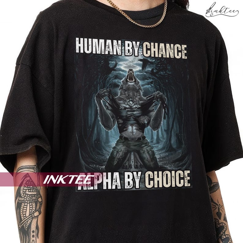 Puede incluir: Camiseta negra con un dise&ntilde;o de hombre lobo transform&aacute;ndose, sobre un fondo de bosque oscuro. El texto "HUMAN BY CHANCE" est&aacute; encima de la imagen y "ALPHA BY CHOICE" debajo. La camiseta tiene un corte holgado.