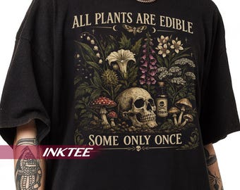 May include: A black t-shirt featuring a graphic print with the text ALL PLANTS ARE EDIBLE SOME ONLY ONCE. The design includes a human skull, various mushrooms, a small bottle labeled POISON, and assorted botanical illustrations in muted tones.