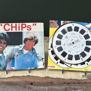Puede incluir: Dos objetos de colección vintage de la serie de televisión "CHiPs". Uno presenta una foto de los actores con el título del programa. El otro es un carrete View-Master con fondo amarillo. Ambos están montados en pequeños soportes.