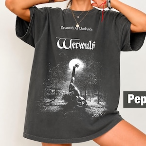 Może przedstawiać: Ciemnoszary t-shirt z krótkim rękawem z białym nadrukiem graficznym przedstawiającym stworzenie sięgające w stronę pełni księżyca na cmentarzu. Tekst "Devoureth All Mankynde" oraz "Werwulf" jest nadrukowany na biało. Widoczne jest słowo "Pepper".