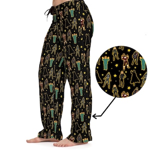 May include: Black pajama pants with a repeating pattern of yellow, green, and red figures on a black background. The figures are silhouetted and appear to be wearing superhero costumes.