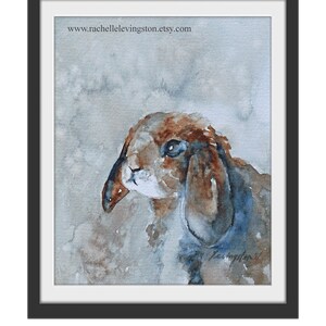K&ouml;nnte beinhalten: Aquarellmalerei eines braunen und wei&szlig;en Kaninchens mit Schlappohren. Das Kaninchen schaut nach links aus dem Bild. Der Hintergrund ist hellblau mit braunen und grauen Aquarell-Waschungen.
