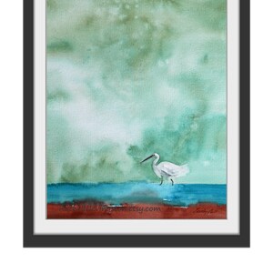 Puede incluir: Pintura acuarela de una garceta blanca de pie en un cuerpo de agua azul con un cielo verde y marr&oacute;n en el fondo. La pintura est&aacute; firmada "Janelle" en la esquina inferior derecha e incluye el sitio web "rachaelevingston.etsy.com" en la esquina inferior izquierda.