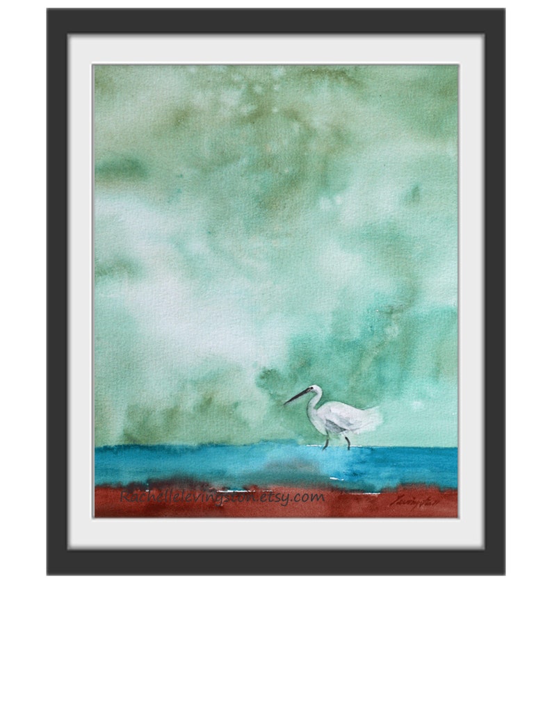 Puede incluir: Pintura acuarela de una garceta blanca de pie en un cuerpo de agua azul con un cielo verde y marr&oacute;n en el fondo. La pintura est&aacute; firmada "Janelle" en la esquina inferior derecha e incluye el sitio web "rachaelevingston.etsy.com" en la esquina inferior izquierda.