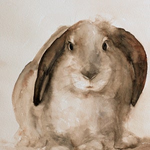 K&ouml;nnte beinhalten: Ein Aquarellbild eines braunen Kaninchens mit Schlappohren. Das Kaninchen sitzt auf einem hellbraunen Hintergrund und schaut direkt auf den Betrachter.
