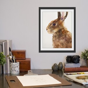 May include: Watercolor painting of a brown rabbit with long ears, looking to the left. The rabbit is painted in shades of brown, with a white background.