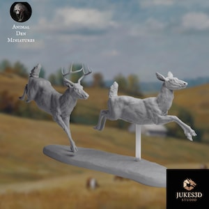 Puede incluir: Dos figuras grises de ciervos en pleno salto, una con cuernos, montadas sobre una base gris. El fondo muestra un paisaje borroso con el texto "Animal Den Miniatures" y "Jukes3D Studio".