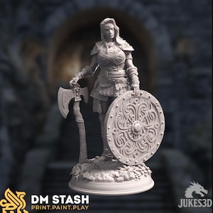 Puede incluir: Figura detallada de una guerrera, sosteniendo un hacha y un escudo. La figura está vestida con una armadura con diseños intrincados. El escudo presenta un patrón circular. La base de la figura tiene el texto "DM STASH PRINT.PAINT.PLAY" y el logotipo de JUKES3D.