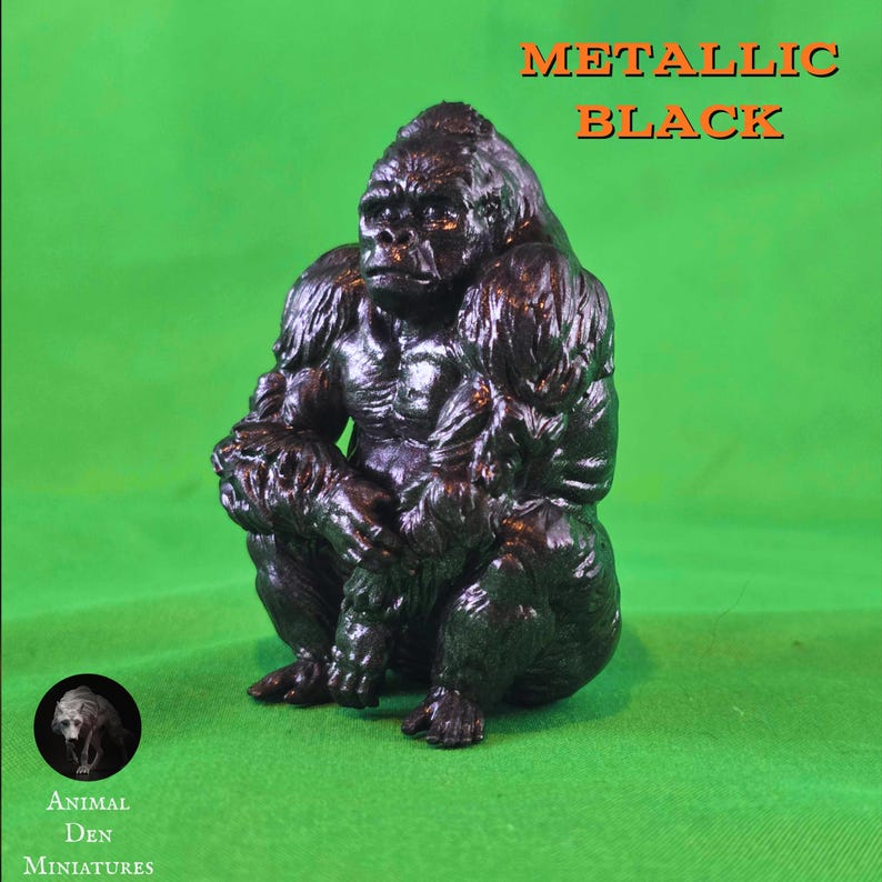 May include: A metallic black gorilla figurine in a seated position. The sculpture has a textured surface and is set against a green backdrop. The text "METALLIC BLACK" is displayed above the gorilla. The logo for "Animal Den Miniatures" is in the lower left corner.