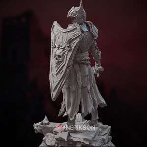 Op de afbeelding: Een gedetailleerd, grijs, 3D-geprint miniatuur van een ridder in volledige bepantsering, die een zwaard en schild vasthoudt. Het schild is versierd met een schedel en ingewikkelde ontwerpen. De ridder staat op een rotsachtige basis.