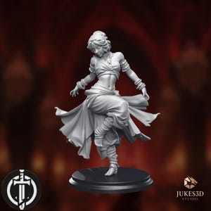 Puede incluir: Una figura miniatura de resina gris de una persona bailando en movimiento, con un top corto, falda de capas y brazaletes. La figura se apoya sobre una base circular negra. El texto JUKES3D STUDIO es visible en la esquina inferior derecha.