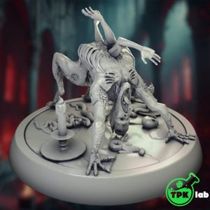 May include: A gray, detailed sculpture of a monstrous creature with multiple limbs and a gaping mouth. The figure is posed on a circular base, with a candle and other grotesque elements. The sculpture has a horror theme.