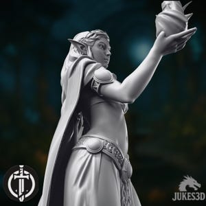 May include: A 3D-printed figurine of an elven woman, holding a decorative object. The figure is wearing a flowing gown and cape, with detailed belt and armbands. The image has a dark background. The JUKES3D logo is visible in the bottom right corner.