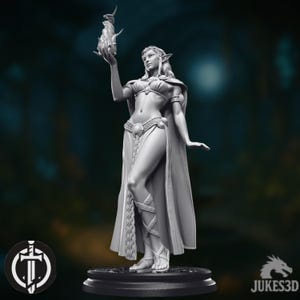 May include: A grey figurine of a female elf holding a flame. The elf is wearing a detailed outfit with a cape, skirt, and sandals. The figurine is on a round base, with a logo in the lower left corner and the text "JUKES3D" in the lower right.