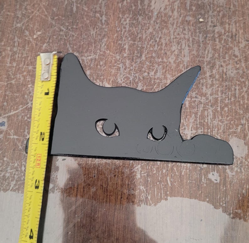 A cute peeking cat decoration shown with a tape measure. The cat appears to be about two and a half inches in height.