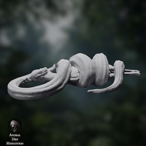 May include: A detailed, grayscale sculpture of a snake coiled around a branch. The snake's body is textured, and its head is visible, with the Animal Den Miniatures logo in the lower left corner. The background is blurred.