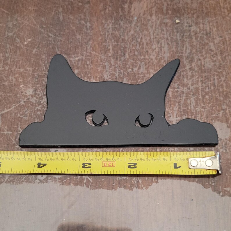 A glossy black peeking cat shown with a tape measure, approximately four and a half inches long.