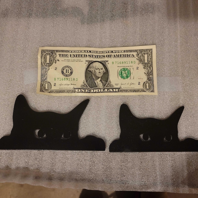 A photo comparing two sizes of decorative cats, side by side compared to a dollar bill.