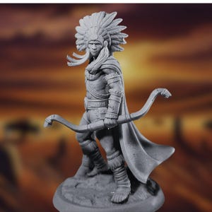 Op de afbeelding: Een grijs geverfd miniatuurbeeldje van een indiaanse krijger met een verenhoed en een boog en pijl in de hand. Het beeldje staat op een ronde voet.