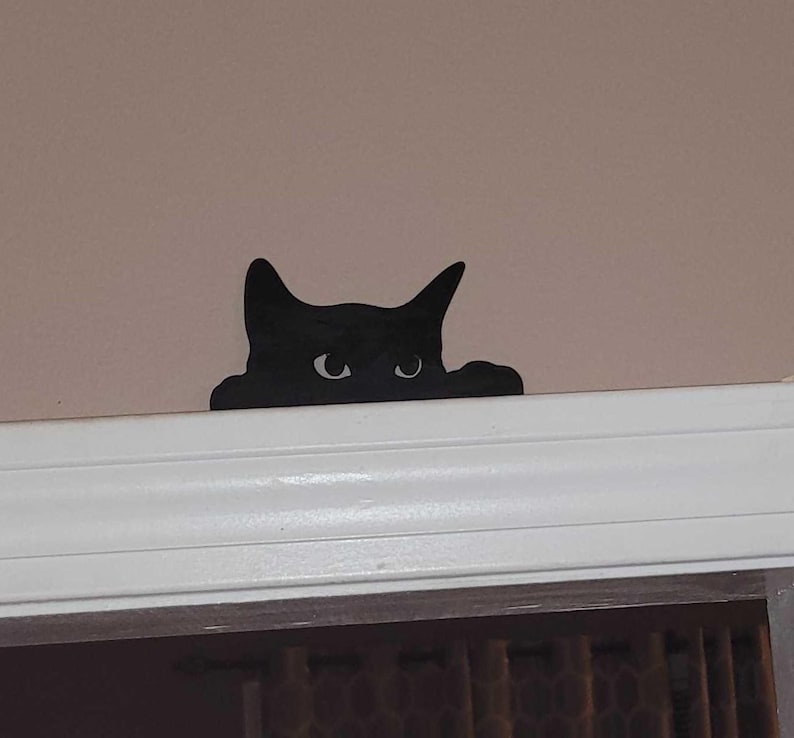 A 3D printed black cat decoration made of resin, designed to appear as if it is peeking over a door frame or shelf edge. The cat has large, detailed eyes and a sleek, smooth finish