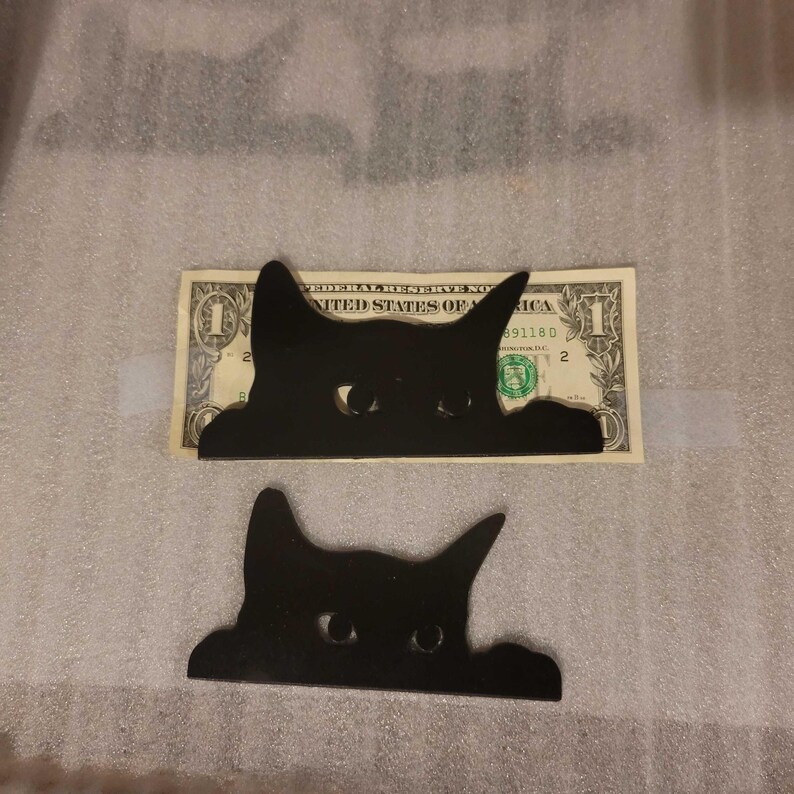 A photo with the larger decorative cat placed on top of the dollar bill. The cat is slightly larger than the dollar bill in height, and only slightly shorter in length.