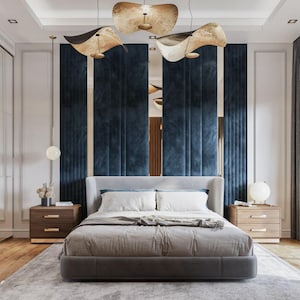 May include: A modern bedroom featuring a gray upholstered bed with white bedding and a gray blanket. Two wooden nightstands with drawers flank the bed. The headboard is against a wall with navy blue panels and gold accents. Decorative lighting fixtures hang from the ceiling.