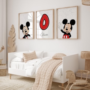 May include: Three framed prints featuring Mickey Mouse and a red number 0. One print shows Mickey Mouse smiling, another shows the number 0, and the third shows Mickey Mouse giving a peace sign. The prints are above a white bed with a beige comforter.