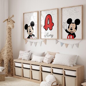 May include: Three framed Mickey Mouse art prints with a wooden frame. One features Mickey smiling, another shows the letter "A" in red with the name "Avery", and the third shows Mickey giving a peace sign. A woven giraffe and storage bench are also in the room.
