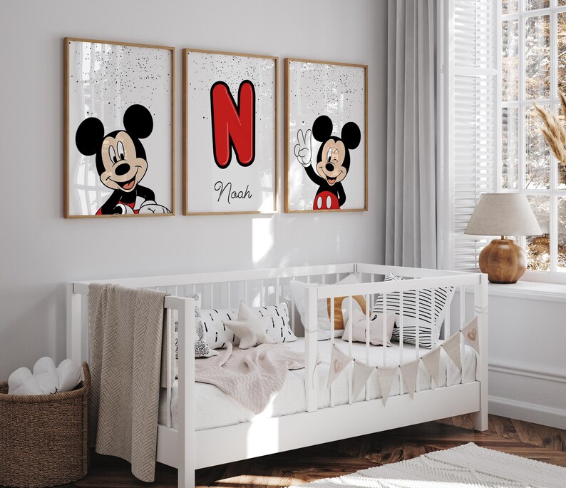 May include: Three framed Mickey Mouse art prints. One features Mickey smiling, another displays a red letter "N", and the third shows Mickey giving a peace sign. The name "Naah" is written below the letter "N". The prints are displayed above a white crib.