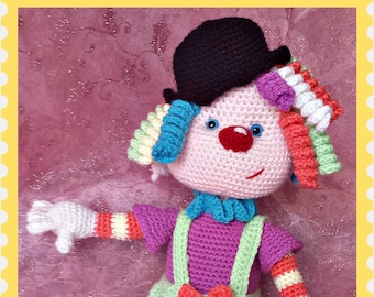 May include: A crocheted clown doll with a black hat, colorful hair, and a purple shirt. The doll is wearing green pants with a red bow and white and red striped legs.