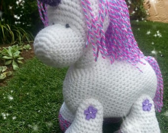 May include: A white crocheted unicorn with a purple and pink mane and tail. The unicorn has purple flowers on its legs.
