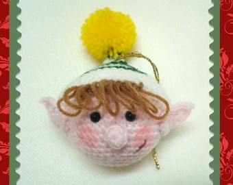May include: A crocheted elf ornament with a pink face, brown hair, and a green and white hat topped with a yellow pom-pom.