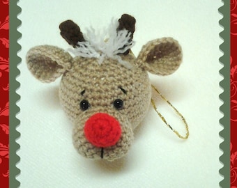 May include: A crocheted reindeer ornament with a red nose, brown antlers, and black eyes. The ornament is hanging from a gold string.