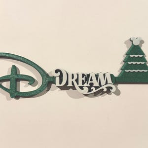 May include: A green and white decorative key with the word "DREAM" in the center. The key features the iconic Disney logo and a Christmas tree design on the end.