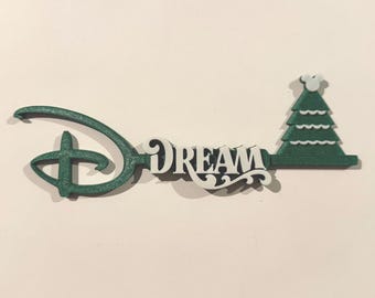 May include: A green and white decorative key with the word "DREAM" in the center. The key features the iconic Disney logo and a Christmas tree design on the end.