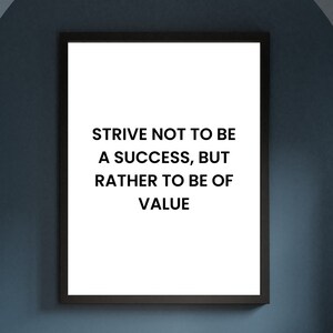 Puede incluir: Una impresión enmarcada con el texto "STRIVE NOT TO BE A SUCCESS, BUT RATHER TO BE OF VALUE" en letras negras sobre un fondo blanco. El marco es negro y la impresión cuelga de una pared azul sobre un suelo de madera.